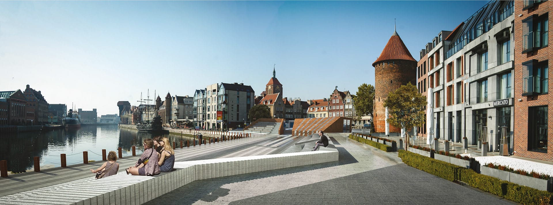 Waterfront panorama with people seated on stepped concrete benches, the promenade, a historic brick tower and townhouses